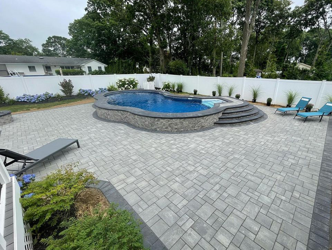 A flagstone path meanders through a backyard oasis, passing by a sparkling pool and lush greenery.