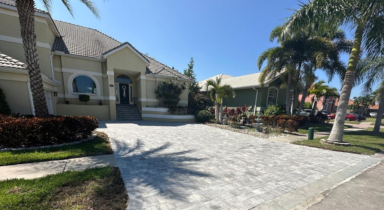 Front yard with a light gray paver driveway and palm landscaping, built using durable materials considered the best pavers for driveways in Florida.