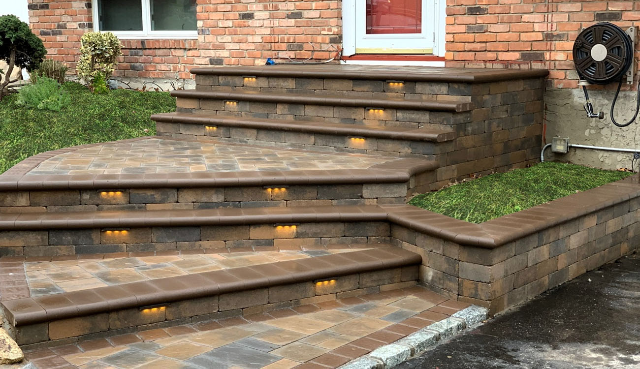 Multi-level front entrance with curved paver steps, built-in LED step lights, and custom stonework from a detailed paver steps installation project