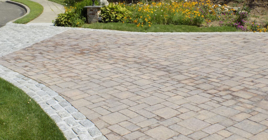 Residential driveway with tan pavers and granite edging, showing a clean and timeless look using the best pavers for driveways in New Hampshire.