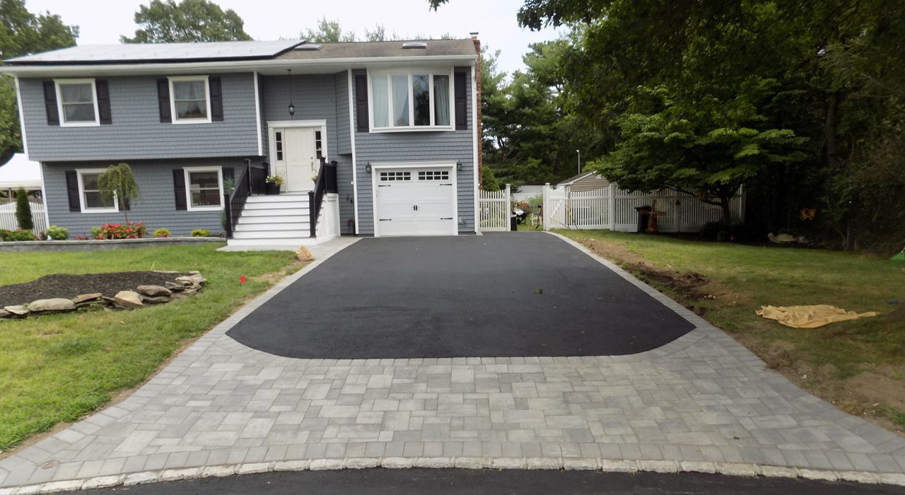 Home with asphalt driveway framed by gray paver apron, demonstrating a durable design made with the best pavers for driveways.
