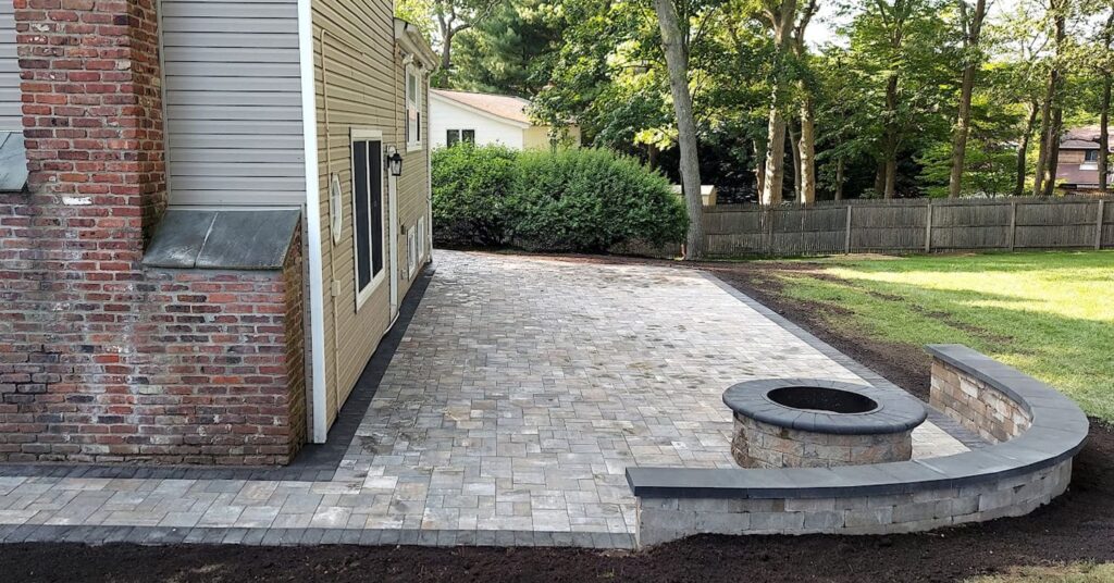 Spacious backyard patio with stone fire pit and seating wall, showcasing one of the best backyard fire pit design ideas for New Hampshire homes