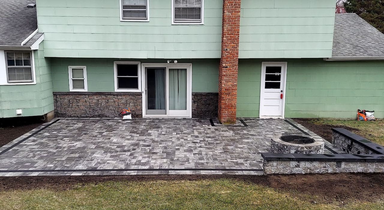 Modern paver patio with built-in fire pit and retaining wall, featuring a clean layout perfect for backyard fire pit design ideas in New Hampshire