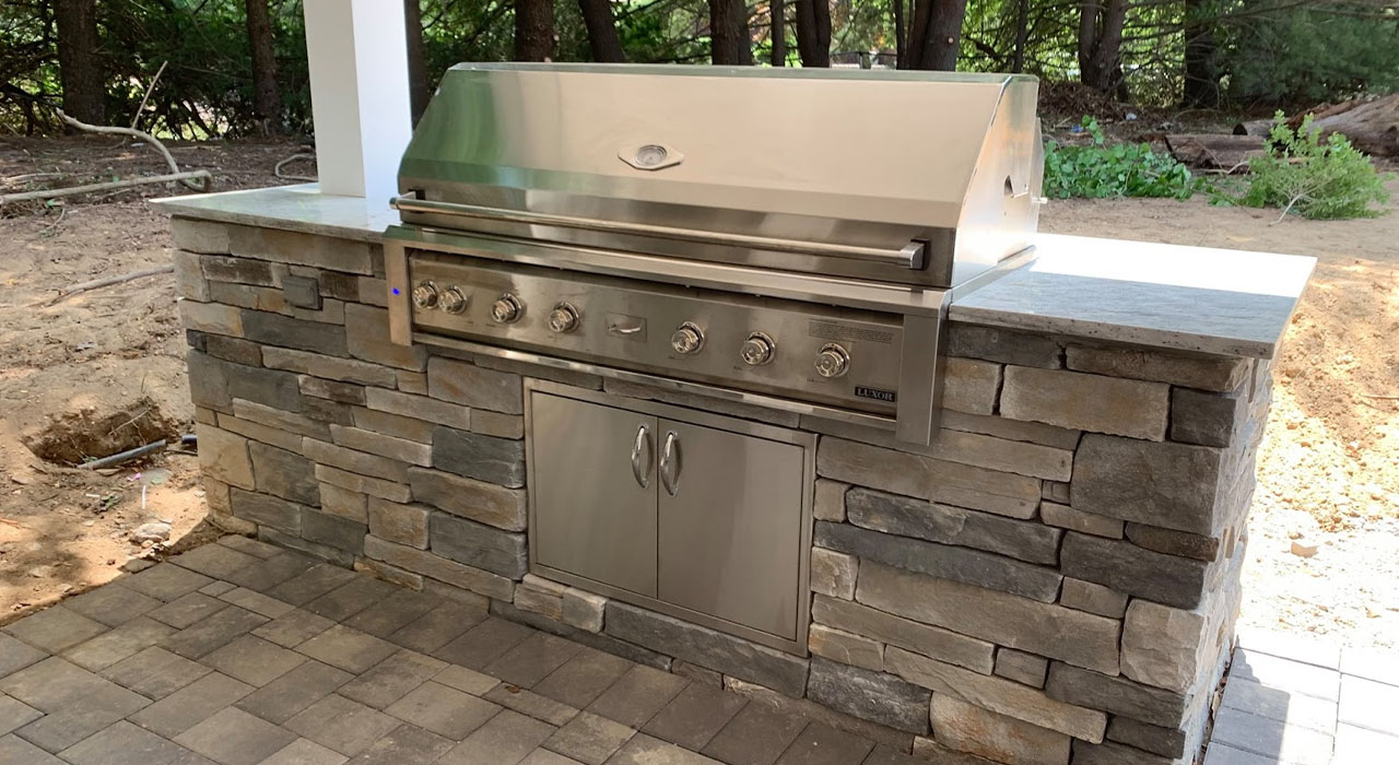 Outdoor stone BBQ island with stainless steel grill built on a custom patio, illustrating material upgrades that affect patio cost per square foot.