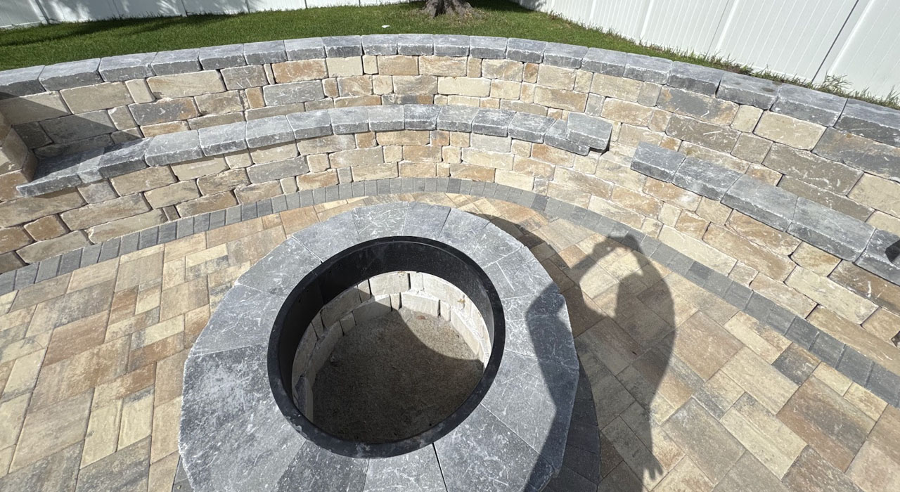 Close-up of stone fire pit surrounded by curved seating wall and detailed paver craftsmanship work.