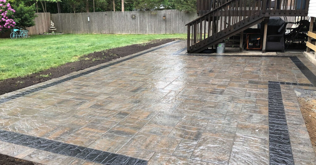 A slate-grey rectangular patio extension designed to complement an existing walkway and white privacy fence.