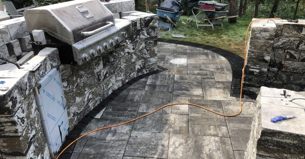 Premium stainless steel grill fitted into a rugged, multi-tonal stone island for professional outdoor cooking.