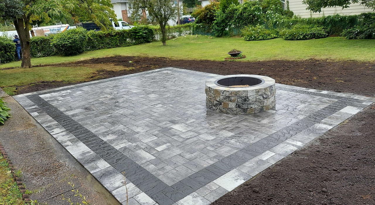 A circular stone masonry unit sits centered on a modern grey and black paver patio.
