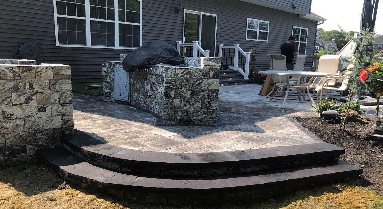 A large-scale stone patio featuring wide steps and an integrated grill station under construction.