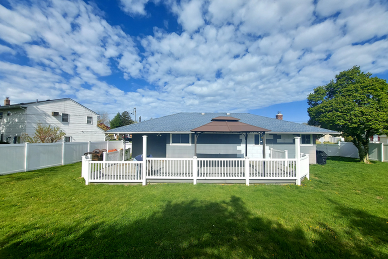 Modern backyard patio in Nassau County featuring large-format gray porcelain pavers and a matching outdoor kitchen area.