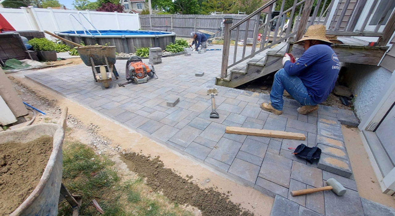 Workers installing a new stone paver patio behind a house.