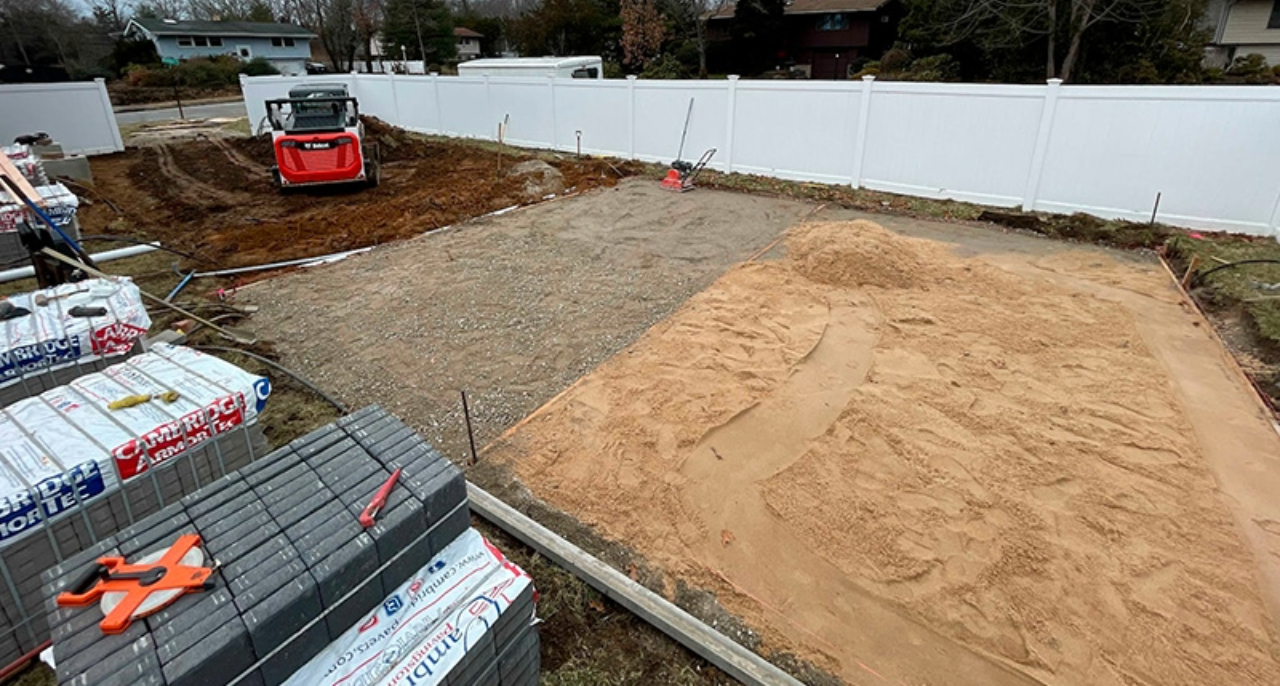 Backyard excavation site prepared with sand and gravel for paving.