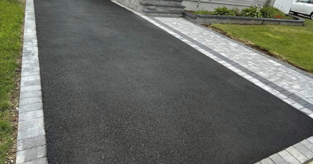 Dark asphalt driveway bordered by decorative light gray stone pavers