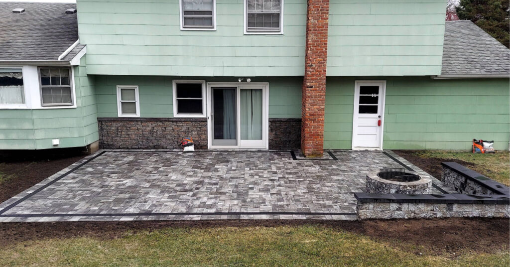A custom grey paver patio featuring a stone seating wall and fire pit, reflecting the cost to install a fire pit.