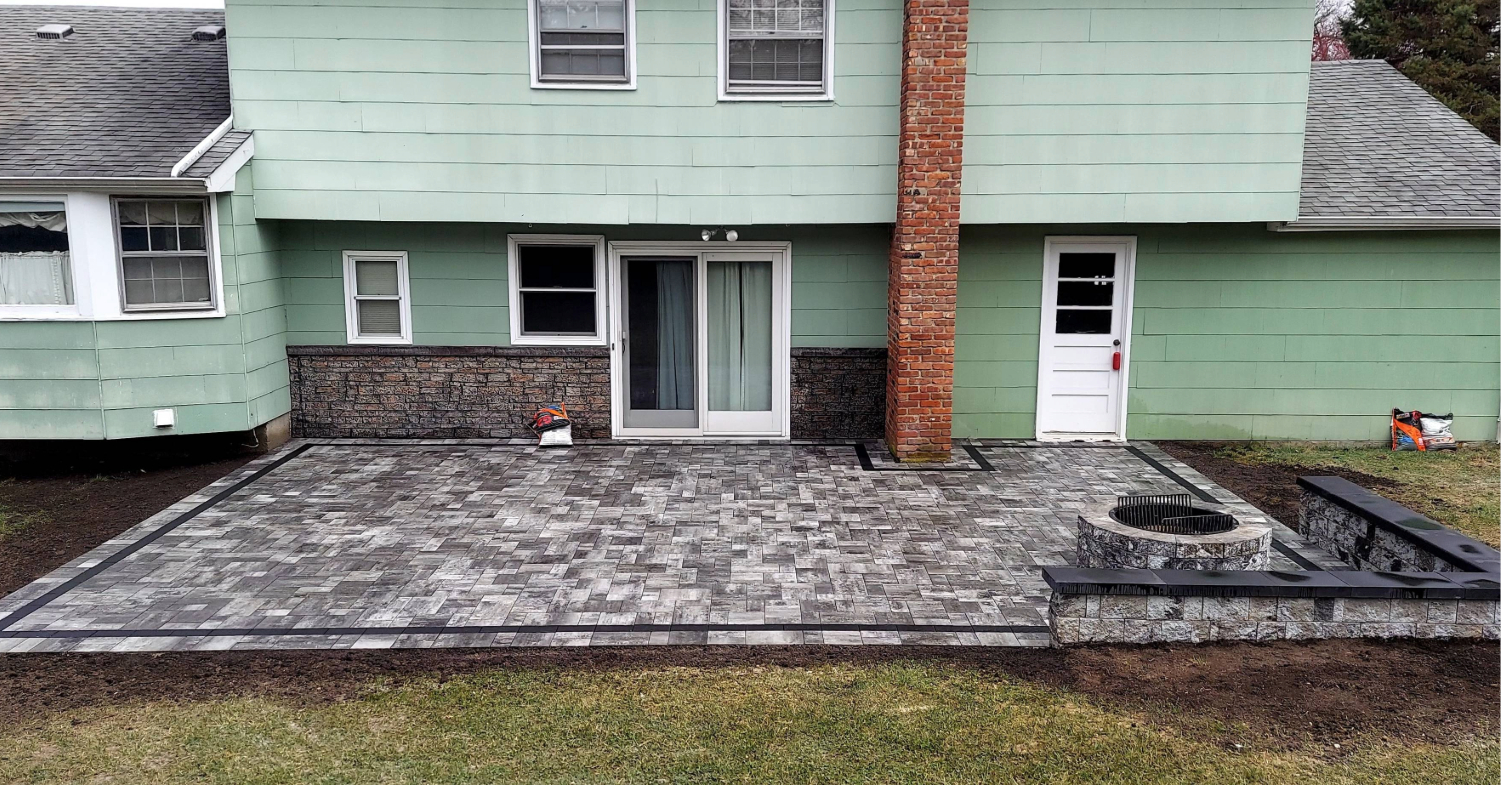A custom grey paver patio featuring a stone seating wall and fire pit, reflecting the cost to install a fire pit.
