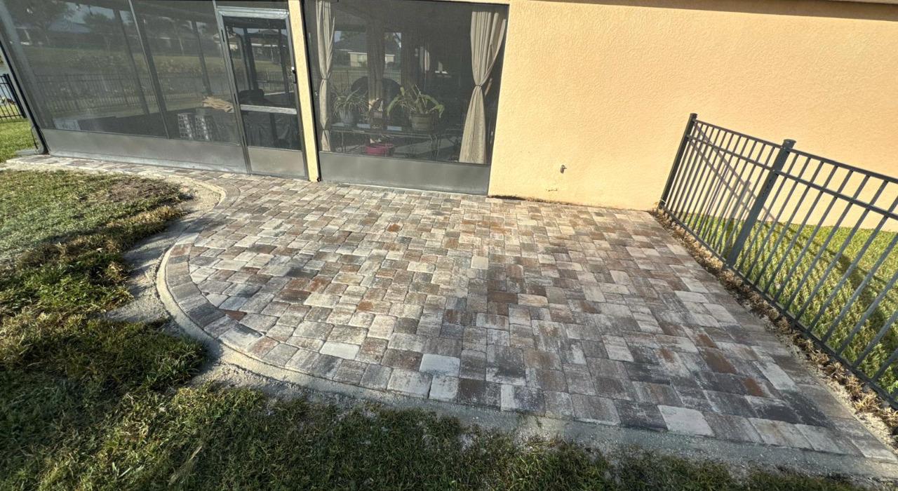 A completed curved paver Patio Installation next to a screened lanai enclosure.