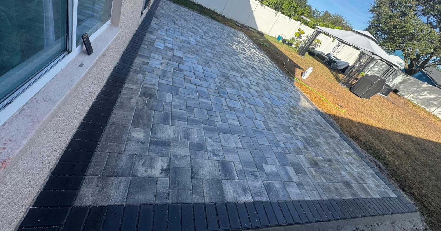 A modern grey paver Patio Installation with a dark border in a Florida backyard.