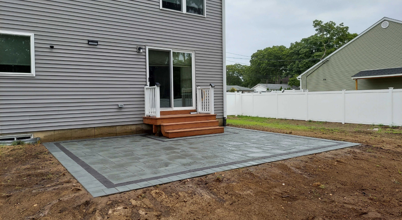 A finished gray stone patio against a home with wood steps, illustrating how long does it take to install a paver patio.