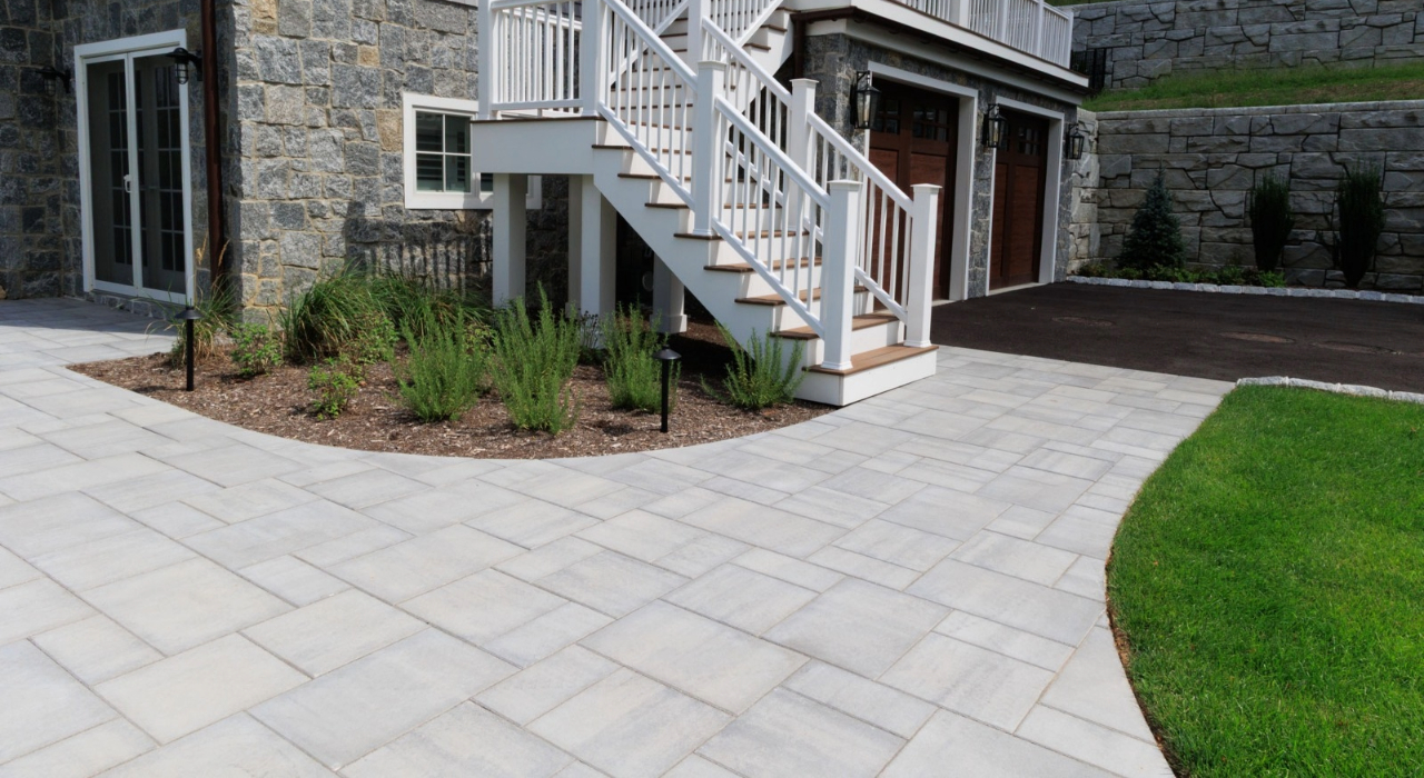 Large, light-colored stone walkway curving past a white staircase and garden, illustrating the cost to install paver walkway.