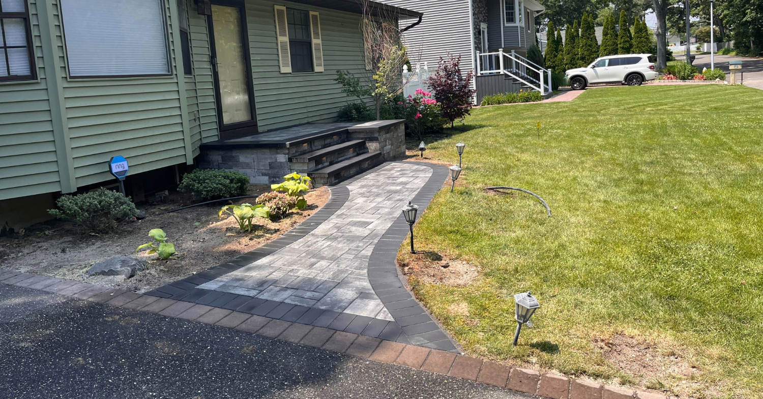 Modern grey stone entrance with dark borders and matching steps, a prime example of the cost to install paver walkway.
