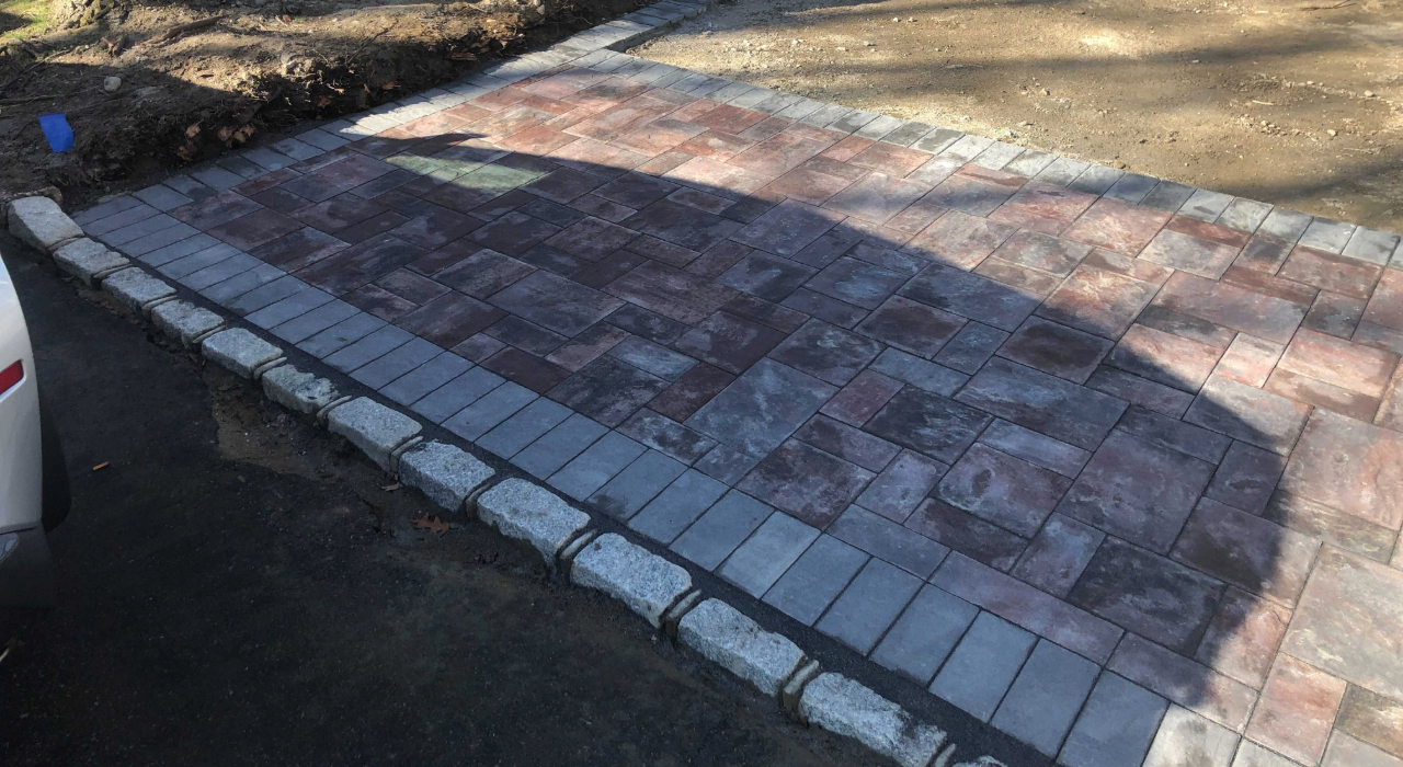 A residential driveway featuring a decorative stone apron and Belgian block curbing, showcasing the best pavers for driveways.