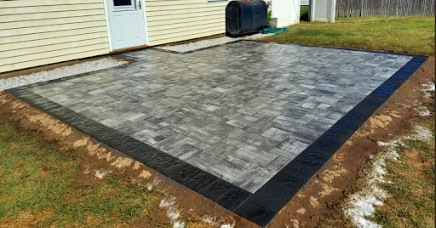 A square grey paver surface built alongside a residential home, showcasing practical enclosed patio design ideas.