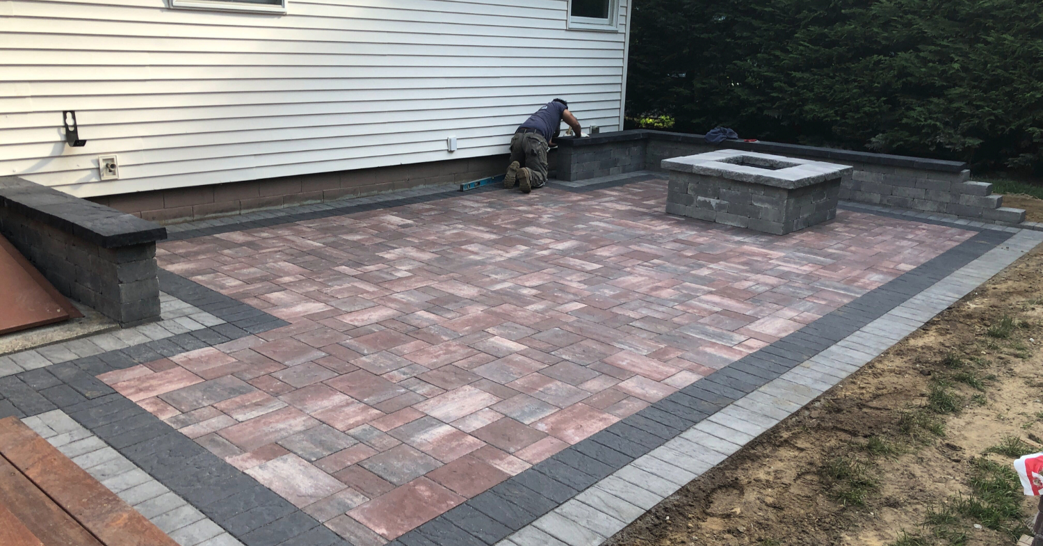 Contractor finishing a square stone fire feature, showing the masonry work required for a natural gas fire pit installation.