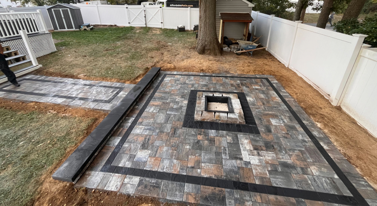 A straight paver walkway leading to a newly built backyard stone area for a fire pit installation.