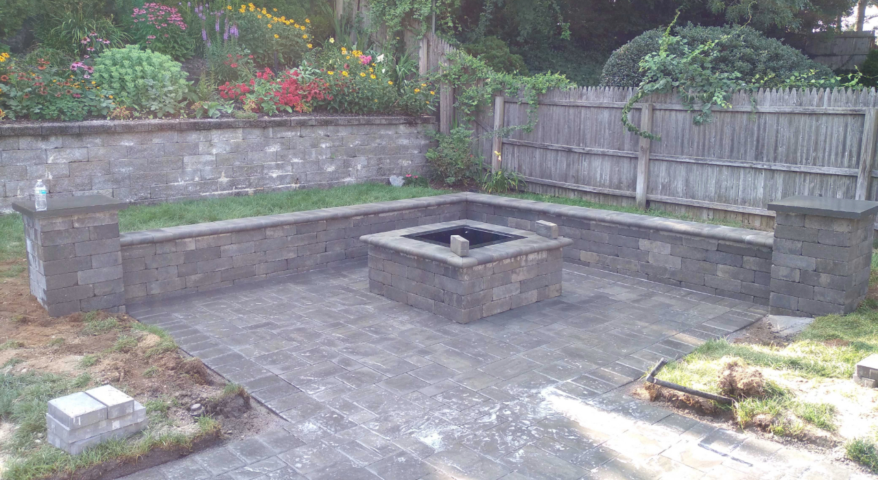 A cozy outdoor seating area featuring a square masonry fire feature, a key factor in fire pit installation cost in Nassau County.