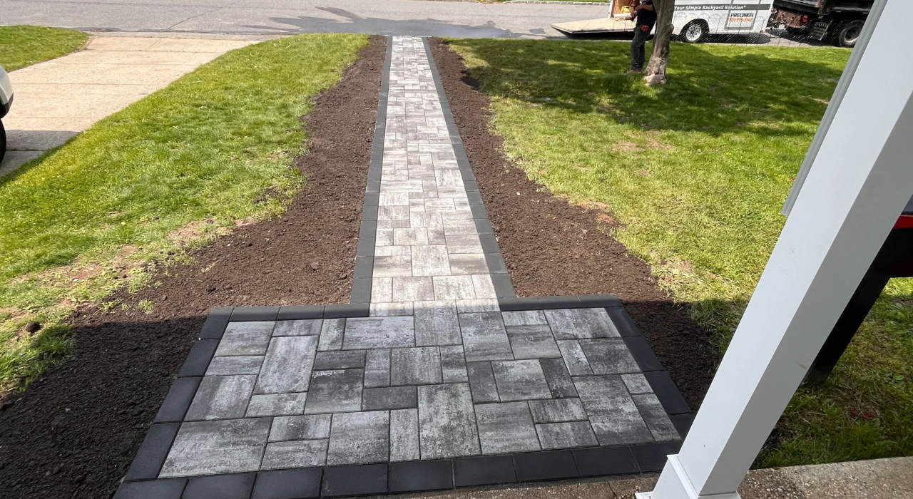 A straight stone path connecting a driveway to the front door, a practical approach to outdoor living space ideas.