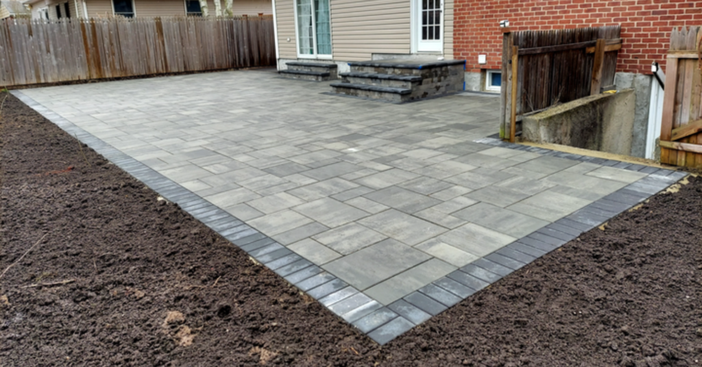 A large, high-end stone seating area with a water view, demonstrating the aesthetic superiority of pavers vs concrete patio.