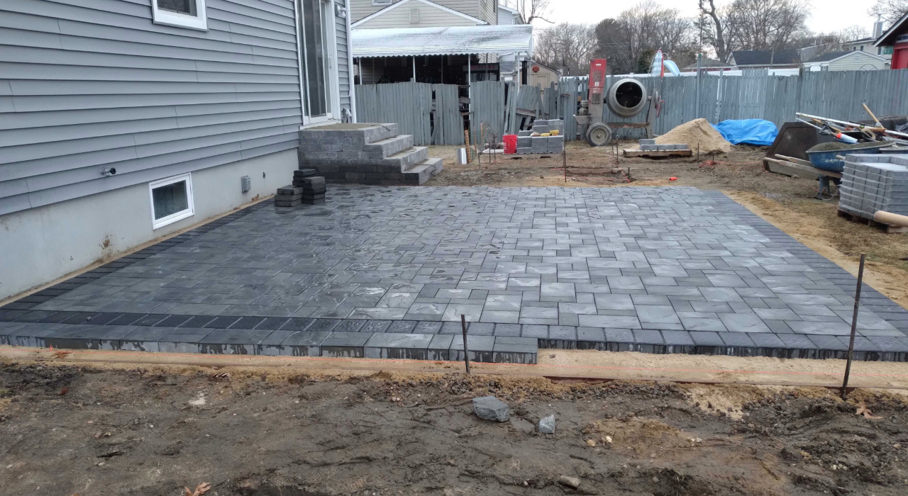 An active backyard construction site showing the intricate stone laying process required for pavers vs concrete patio.