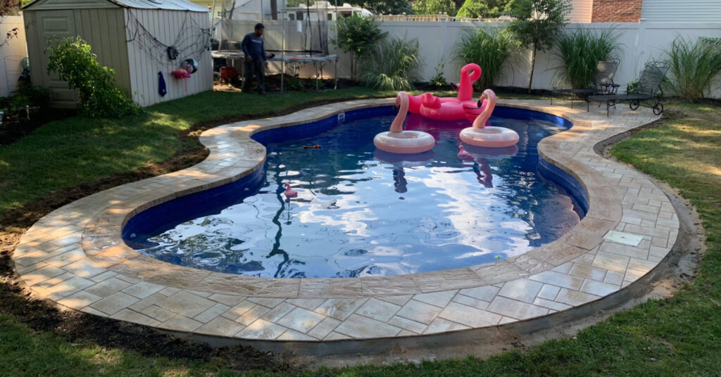 A curved stone deck surrounding a backyard swimming pool, a major factor in the total pool patio cost in nassau county.