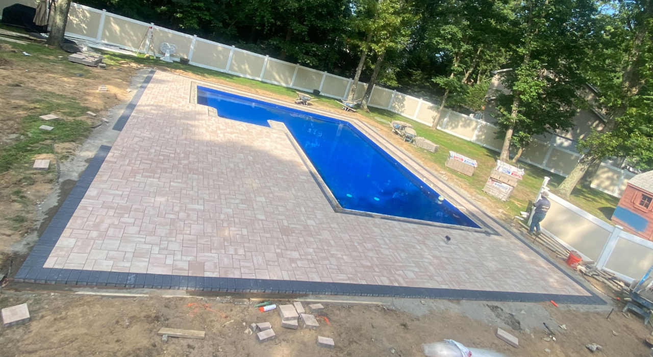 Large scale interlocking paver installation around a rectangular pool, illustrating the typical pool patio cost in nassau county.