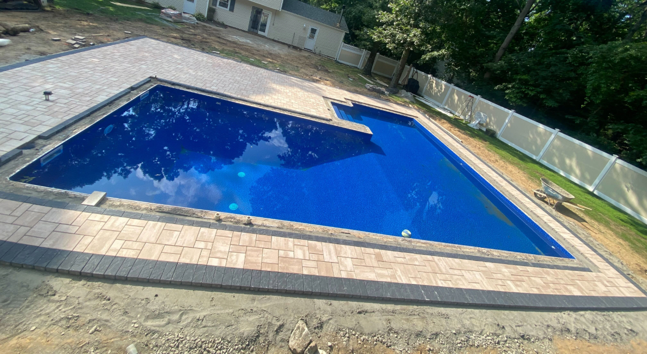 A finished light-colored stone pool surround with dark borders, showcasing premium materials that affect pool patio cost in nassau county.