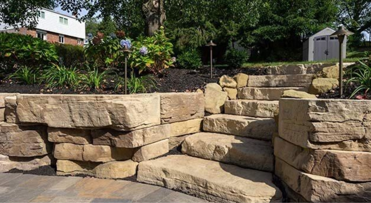A decorative curved stone wall bordering a paver patio, illustrating high-end landscaping options for retaining wall cost in Nassau County.