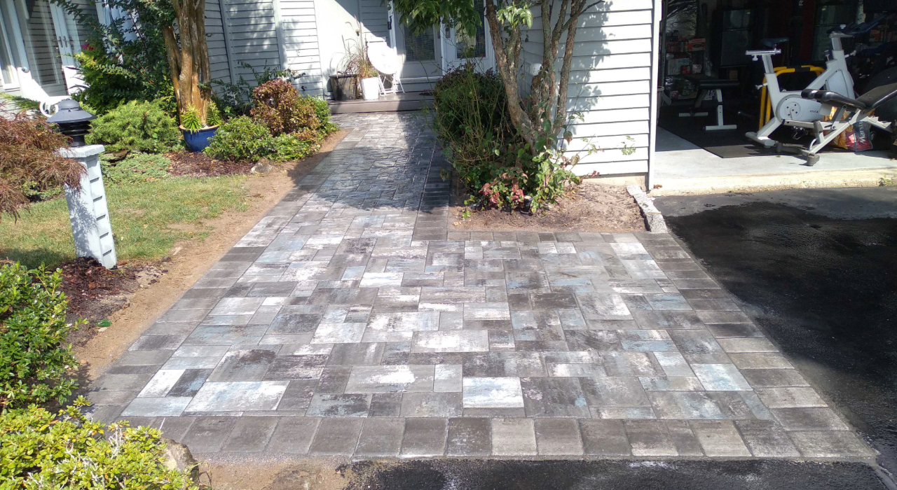 Wide interlocking stone entrance with a professional grey finish, illustrating the results of how to install a paver walkway.