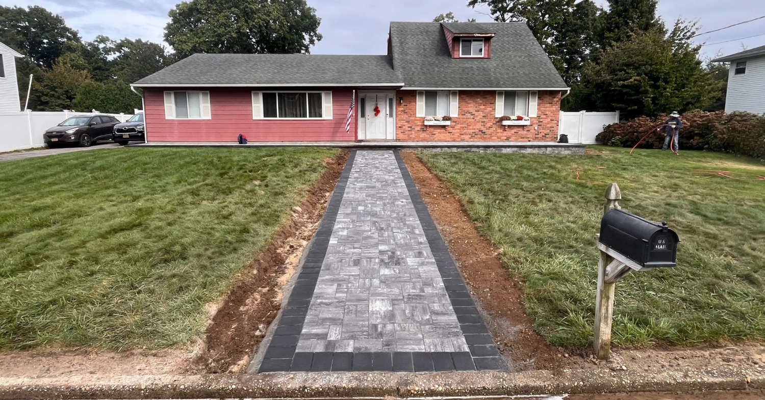 A long, straight paver path leading directly to a front door, showing a newly completed residential walkway installation.