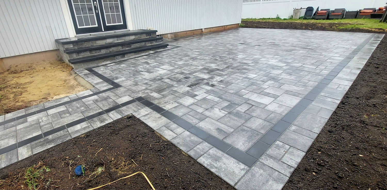 A close-up of stone units being placed onto a level sand bed, a key step in how to install patio pavers.