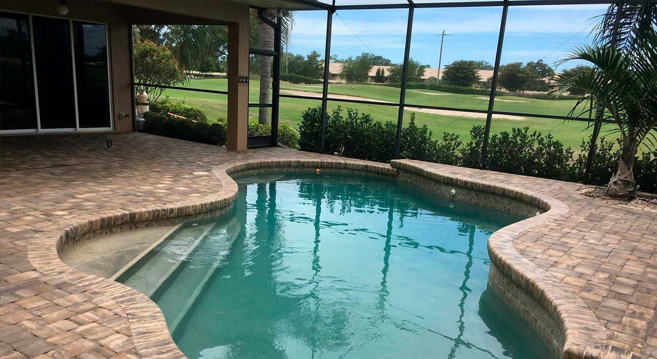A kidney-shaped pool with a textured stone deck, fully integrated into spacious and durable custom pool enclosures.