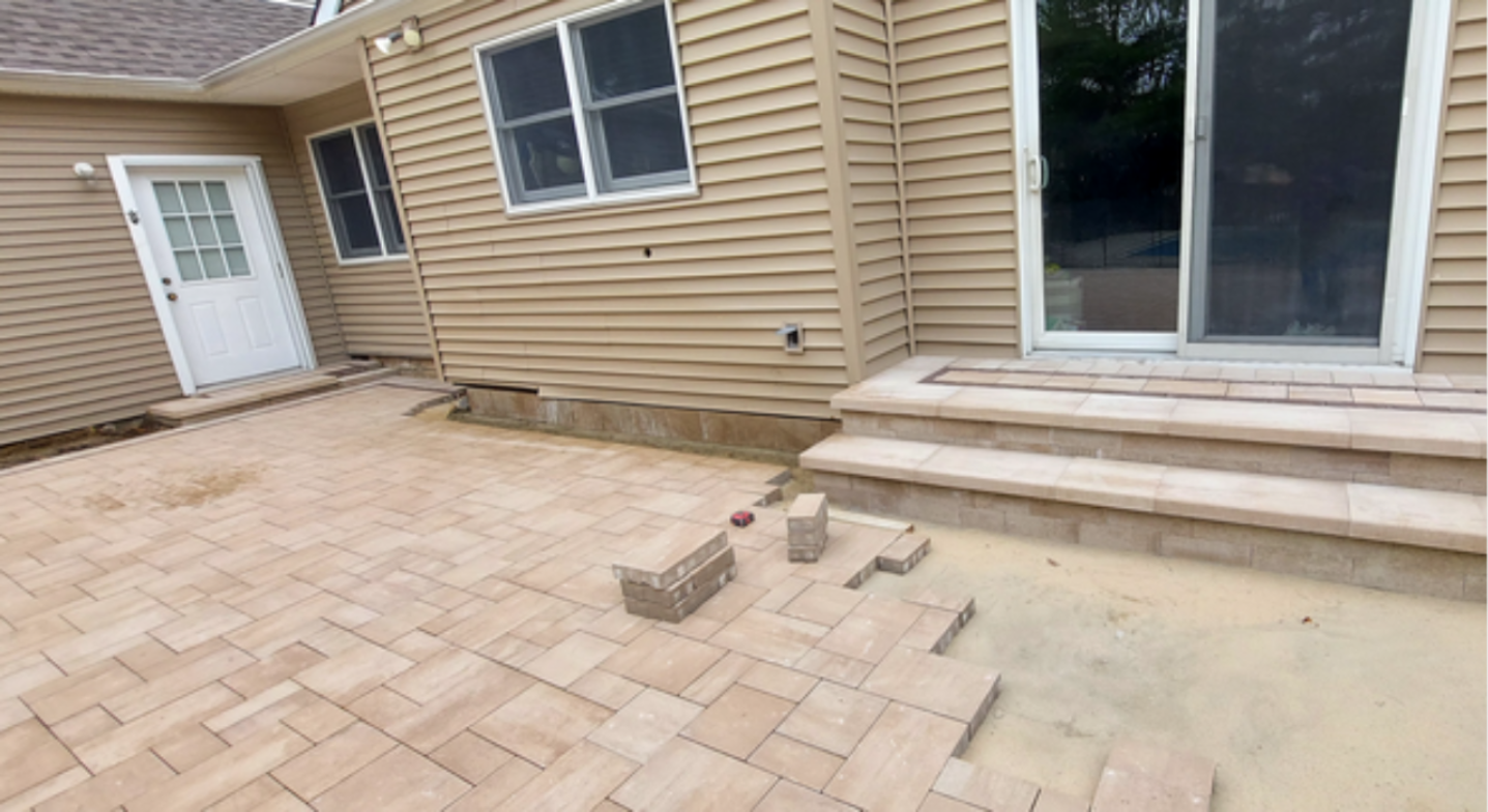 Tan multi-level stone layout with integrated steps, showcasing premium features that affect the cost to install a brick paver patio.