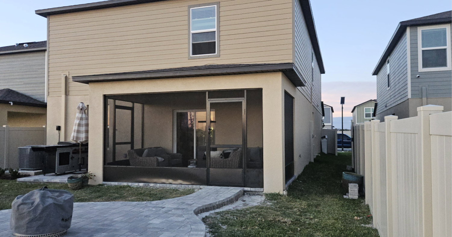 A spacious empty paver patio looks out over lush green grass from inside highly protective and modern lanai screen enclosures.