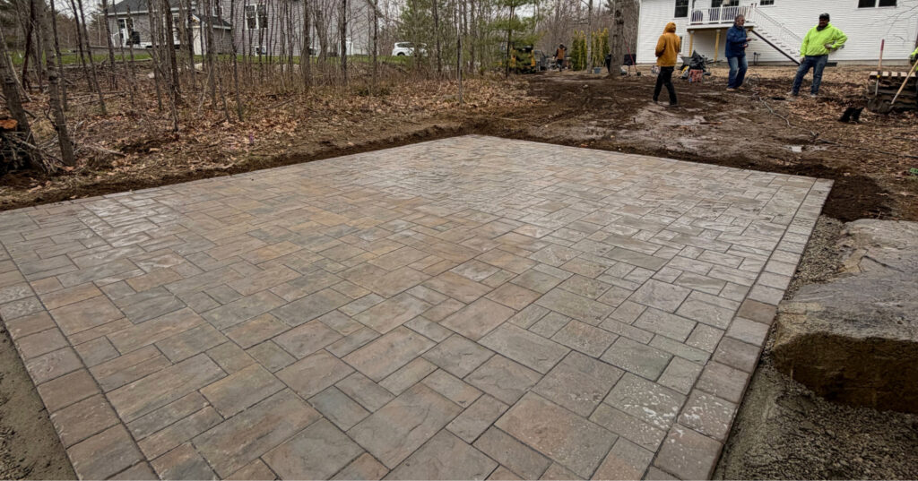 A worker finishes the edges of a new stone surface, perfectly illustrating the paver patio vs concrete patio visual debate.