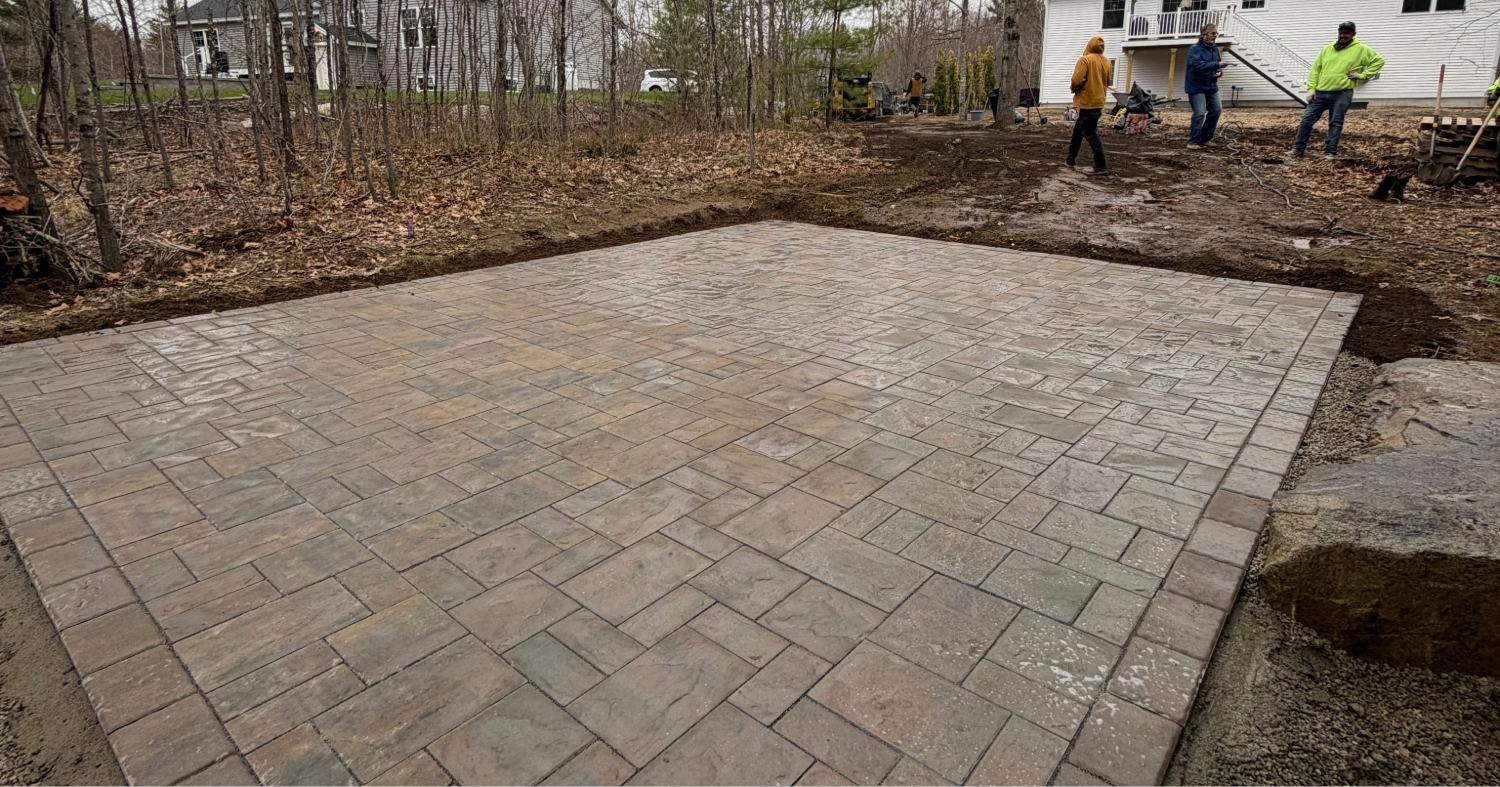 A worker finishes the edges of a new stone surface, perfectly illustrating the paver patio vs concrete patio visual debate.