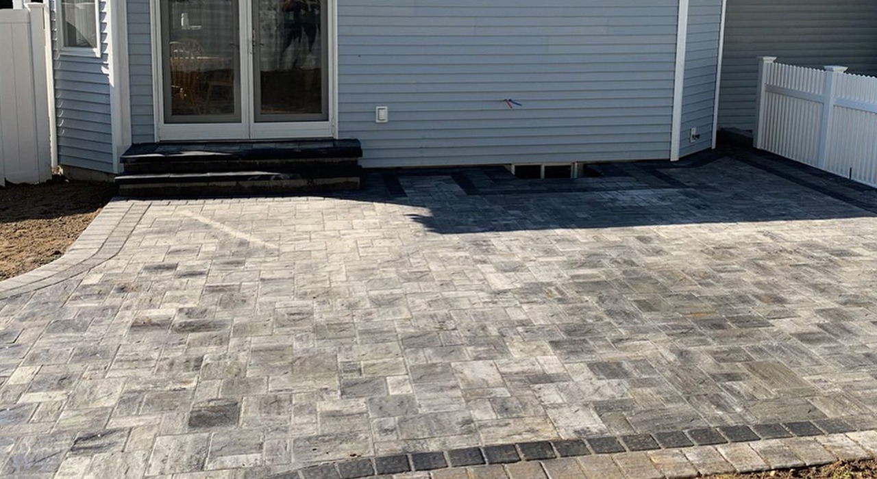 A pristine light-gray backyard stone paver patio installation in Concord with white fencing.