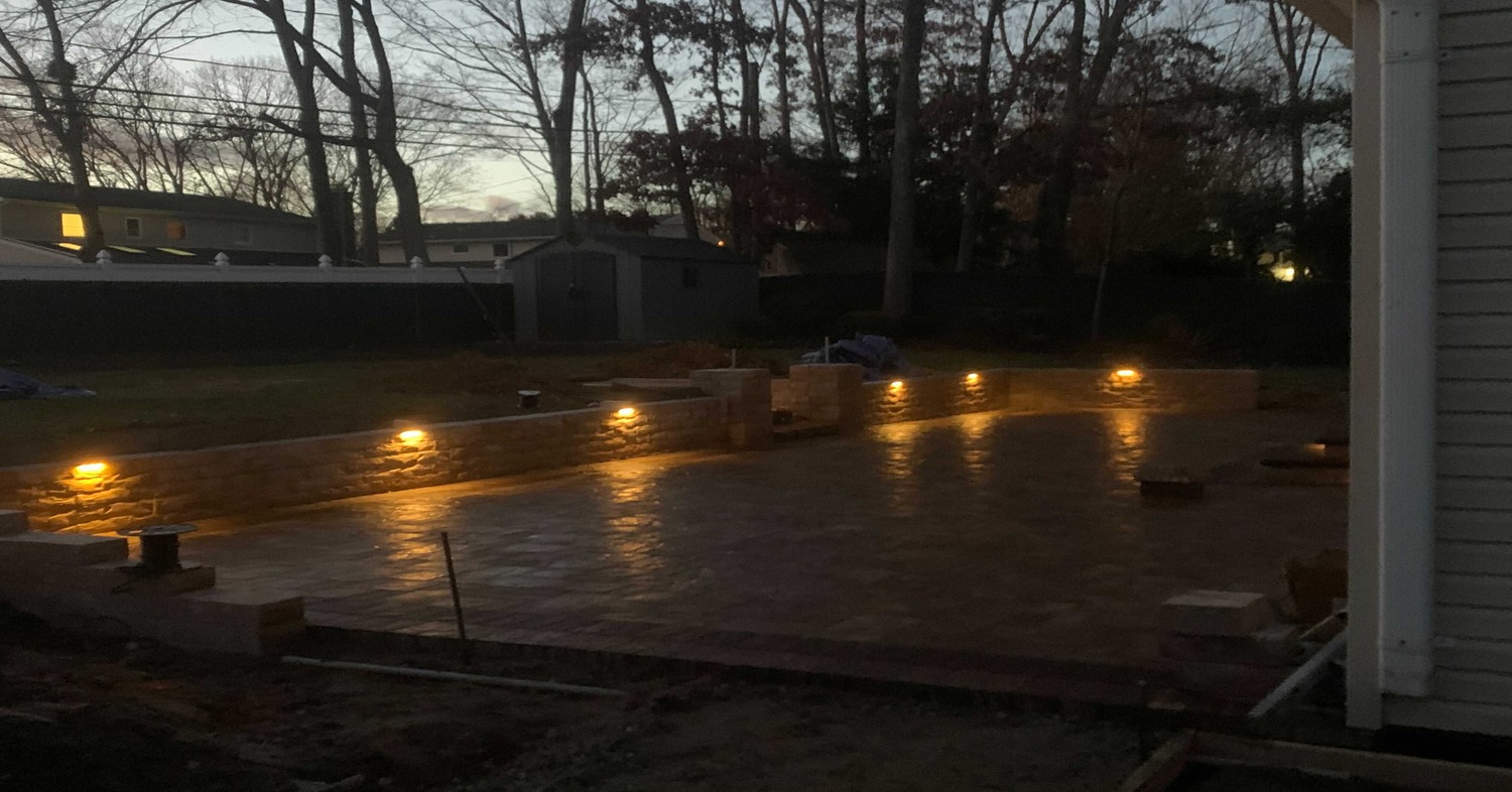 Integrated wall lighting at dusk during a retaining wall installation in Dover.